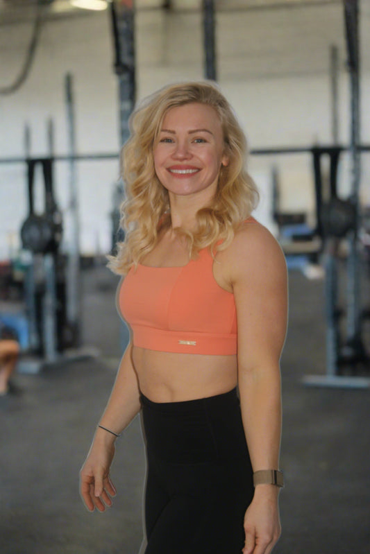CrossFit Girl wearing orange square neck sports bra standing at the front of a CrossFit box