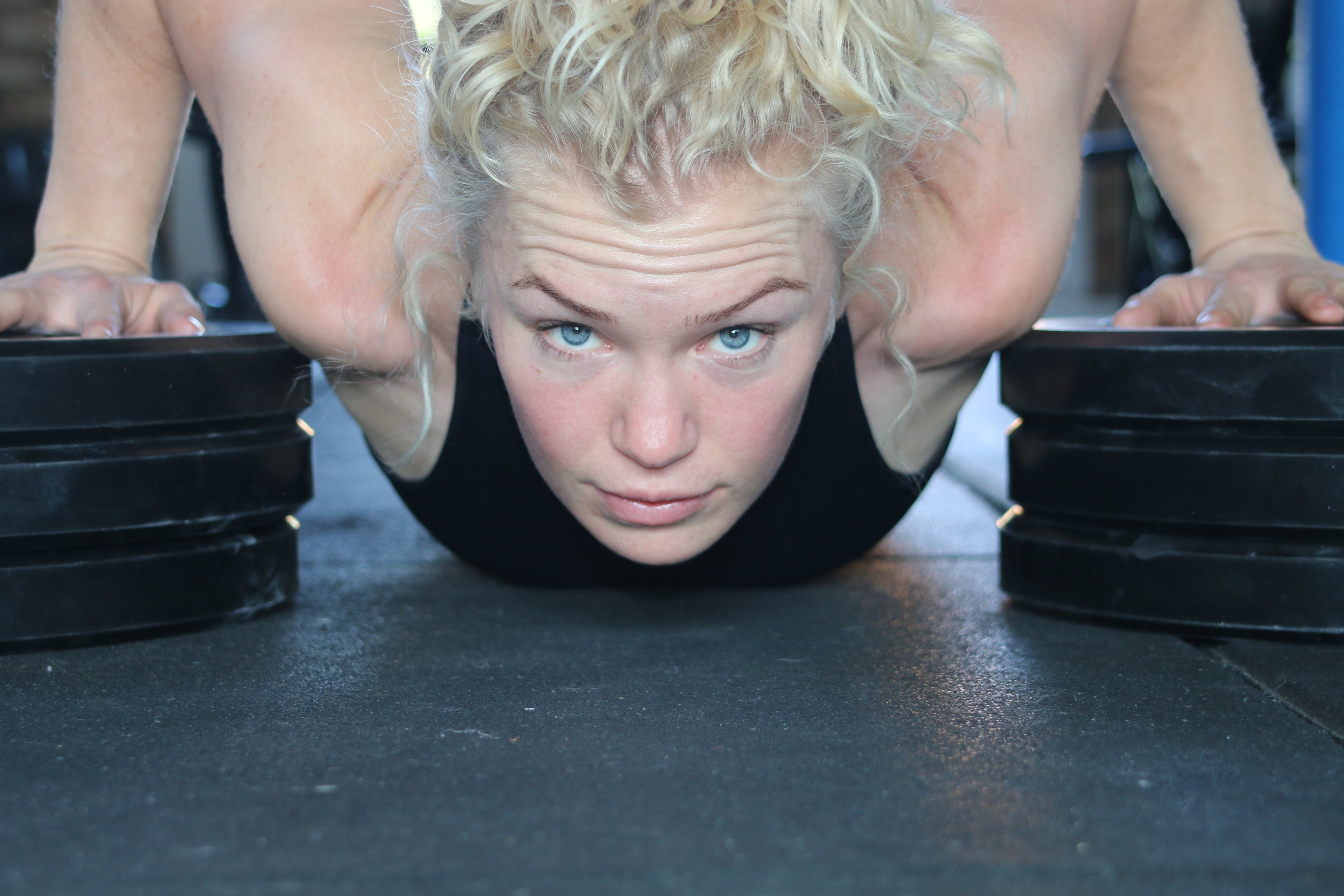 Fitness girl doing deficit push-up on plates looking directly at the camera.