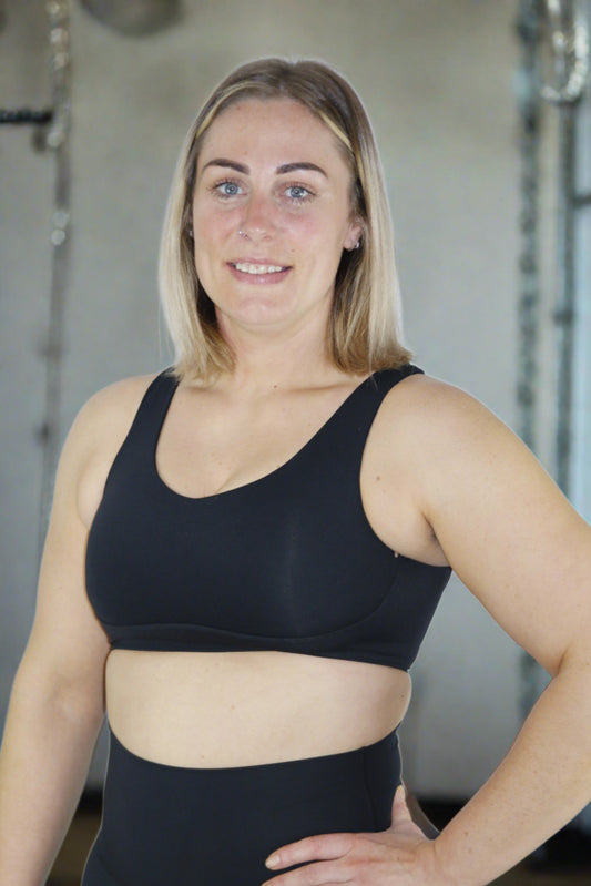 CrossFit girl wearing a black high impact sports bra standing in a CrossFit Gym